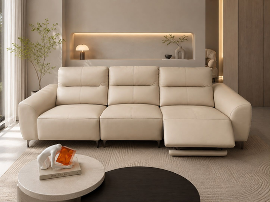 A modern three-seat sofa with a chaise lounge in a minimalist beige living room setting, featuring a round coffee table and a built-in shelf in the background.