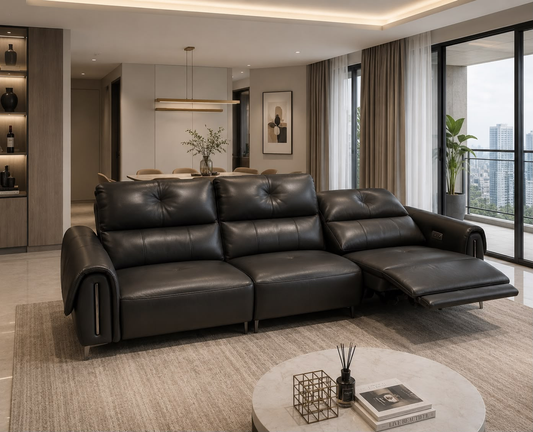 A modern black leather sectional sofa with a chaise lounge extended, shown in a contemporary living room setting with a round coffee table, textured rug, and large windows overlooking a city skyline.